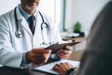 Male doctor holding clipboard and speaking to male patient across a desk