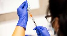 A pharmacy technician wearing blue latex glove and a surgical mask prepares a dose of the Moderna COVID-19 vaccine.