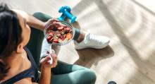 A woman in athletic gear sits while eating a bowl of fruit and oats.
