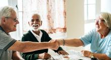 Three senior citizens shaking hands across a table