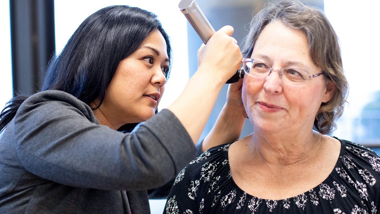 Grace Mausisa, RN, left, a research nurse, conducts a hearing evaluation on study participant Karen Newcomb, part of a clinical trial that assesses hearing damage from chemotherapy. Image by Susan Merrell Doctor examines a patientʻs ear for signs of tinnitus