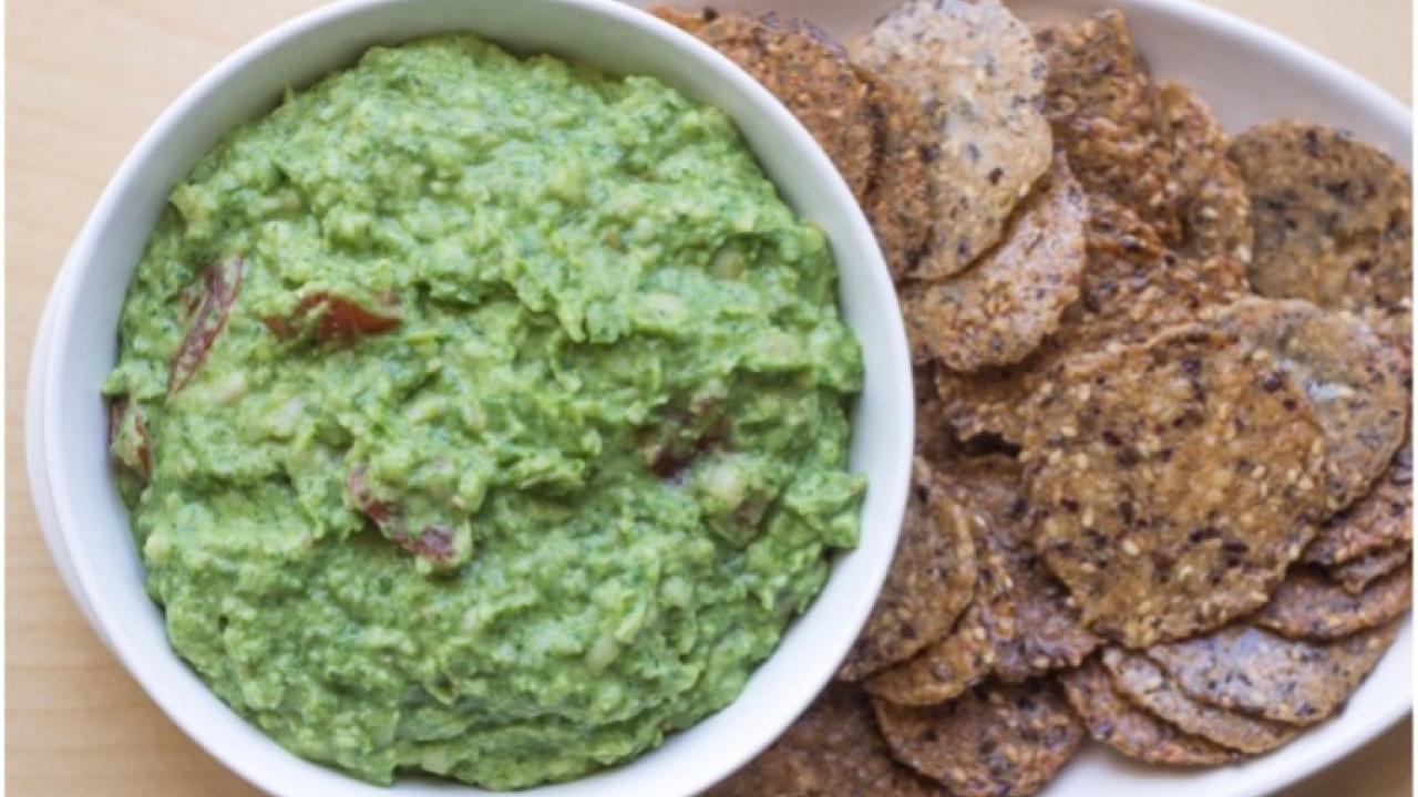 green dip in bowl next to plate of whole grain crackers