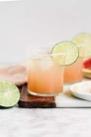 pink-orange beverage served in cocktail glass with lime wheel