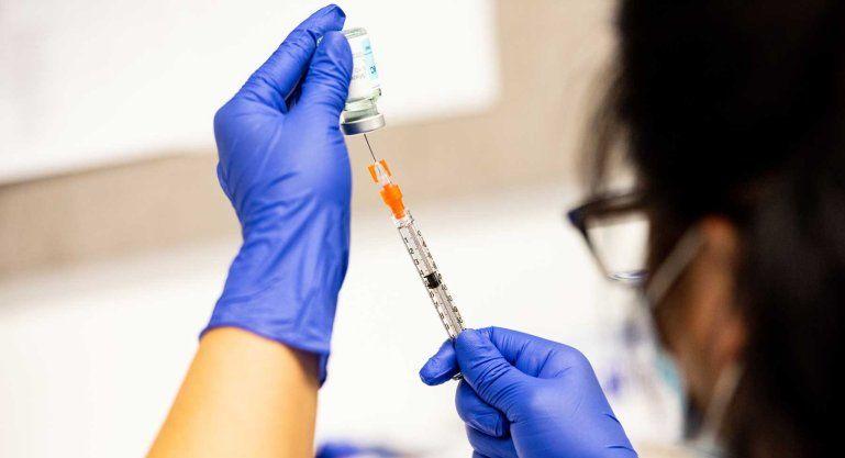 A pharmacy technician wearing blue latex glove and a surgical mask prepares a dose of the Moderna COVID-19 vaccine.