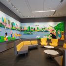 Photo of empty waiting area with bright yellow chairs and a large colorful painting on the wall.