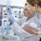 Two lab members in white coats examining samples in pipettes