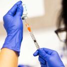 A pharmacy technician wearing blue latex glove and a surgical mask prepares a dose of the Moderna COVID-19 vaccine.